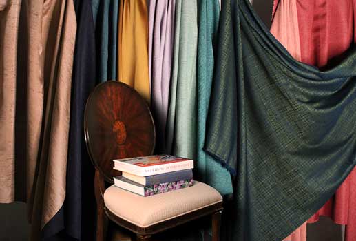 Various colors and shades of drapery fabrics draped behind an accent chair
